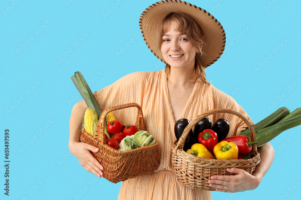 Young female farmer with wicker baskets full of different ripe vegetables on blue background