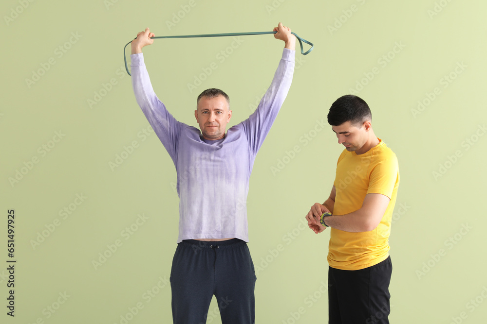 Mature man training with stretching tape and rehabilitation therapist on green background