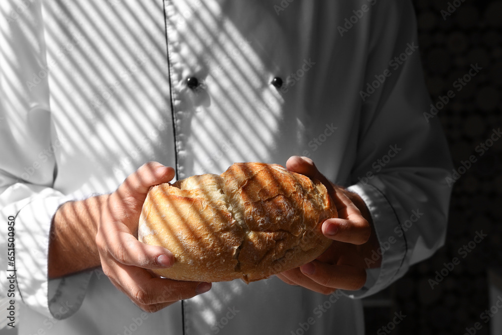 Young chef with loaf of fresh bread in bakery near window