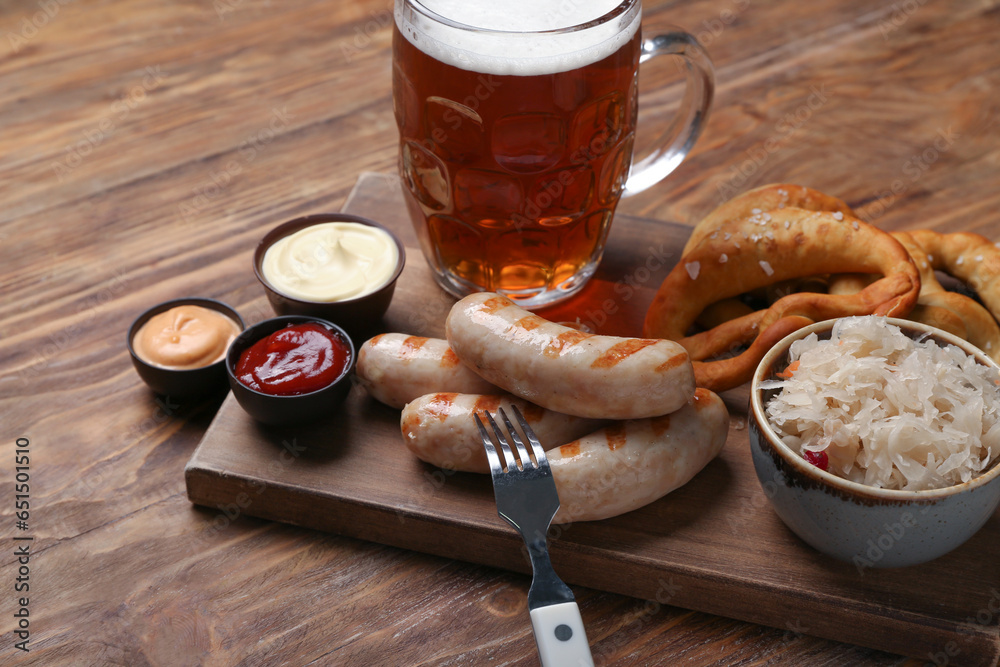 Board with tasty Bavarian sausages, sauces, sauerkraut, pretzels and mug of beer on wooden background. Oktoberfest celebration