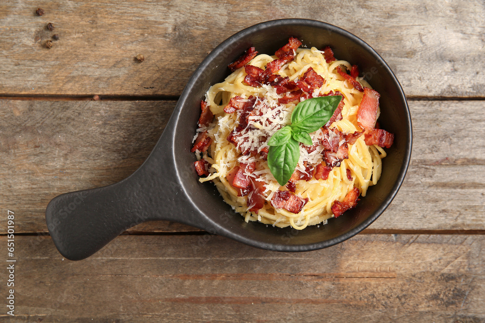 Frying pan with tasty pasta carbonara on wooden background