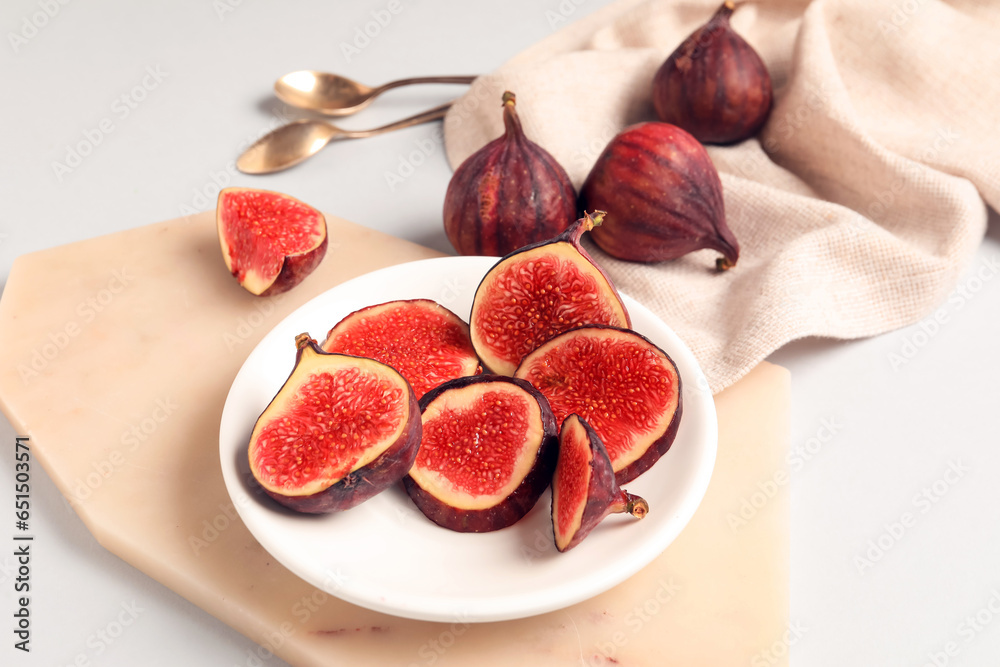 Plate with fresh juicy cut figs and spoons on white background