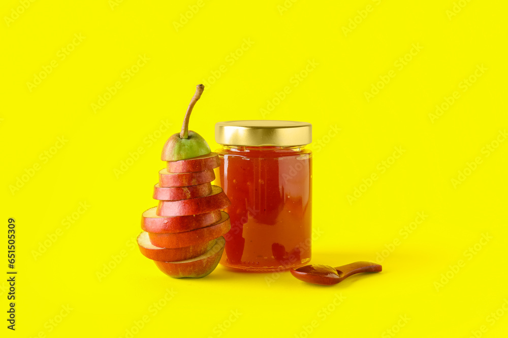 Glass jar of tasty pear jam with wooden spoon on yellow background