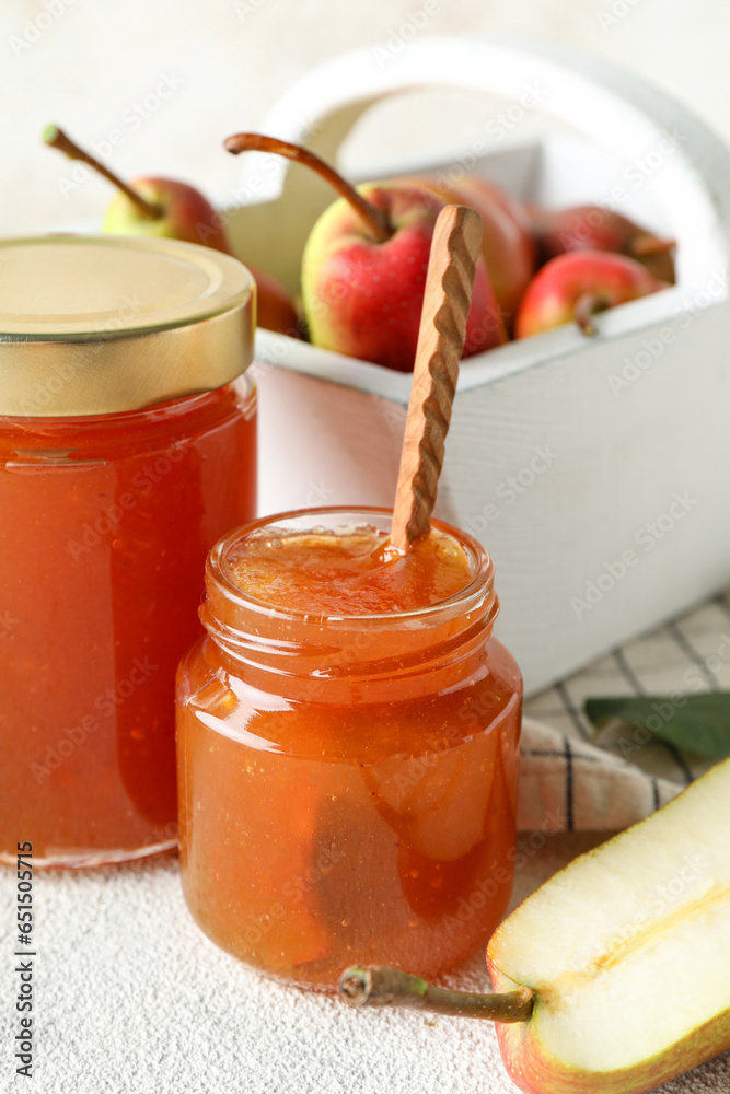 Glass jars of tasty pear jam with wooden spoon on white table