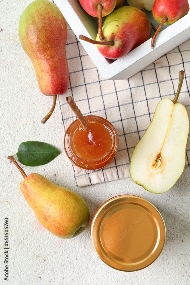 Glass jars of tasty pear jam with basket on white table