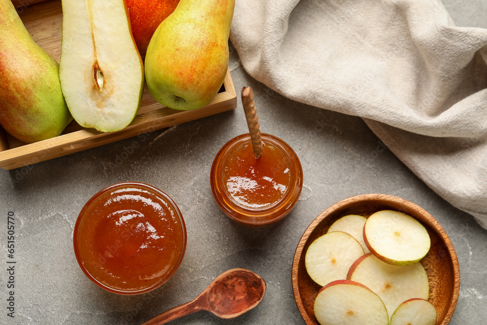 Glass jar and bowl of tasty pear jam with wooden box on grey table