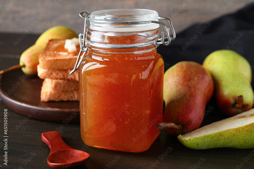 Glass jar of tasty pear jam on wooden background