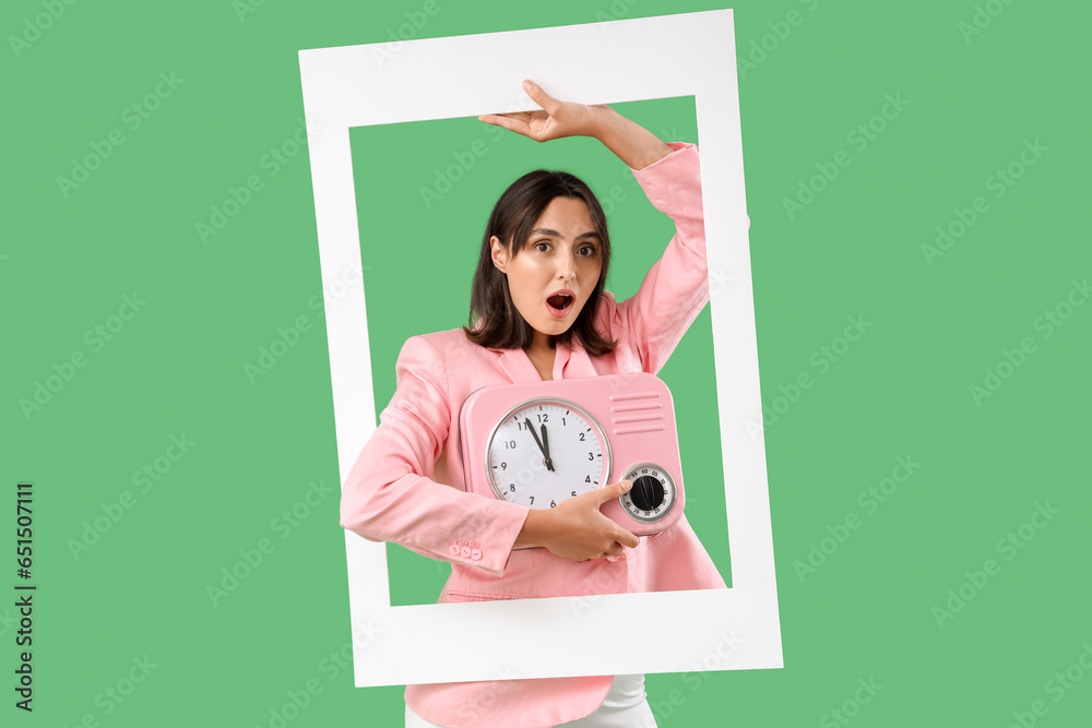 Beautiful young woman with kitchen clock and frame on green background