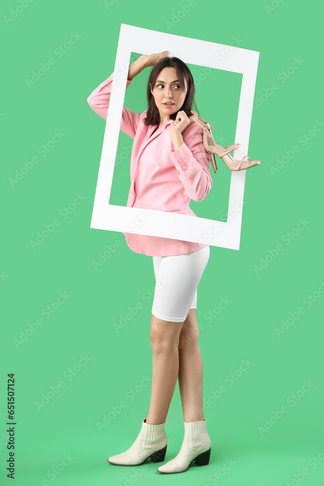 Beautiful young woman with stylish high heels and frame on green background