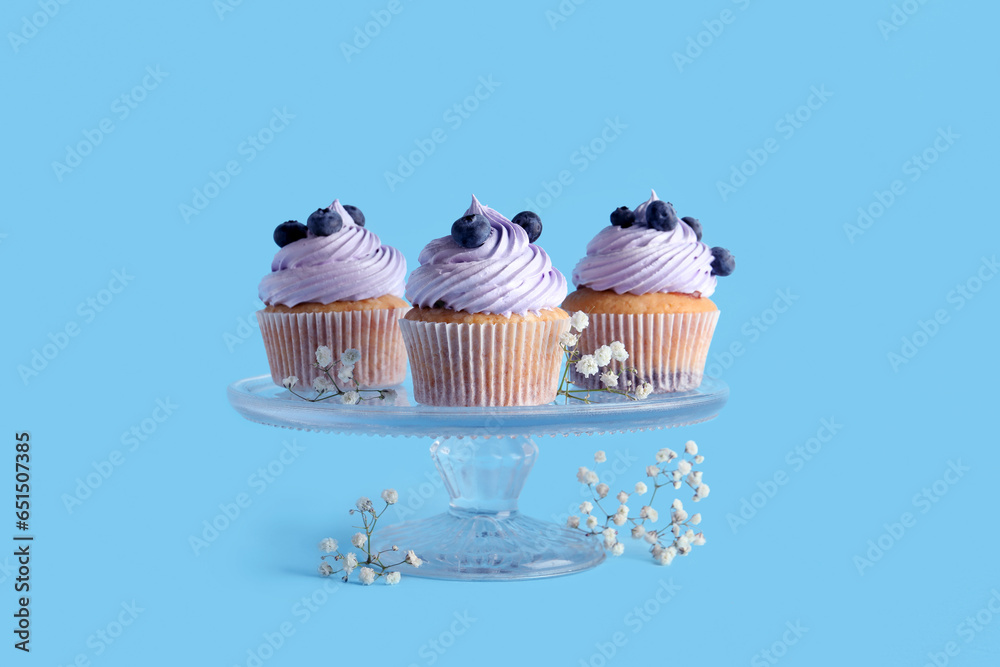 Stand of tasty cupcakes with blueberries on blue background