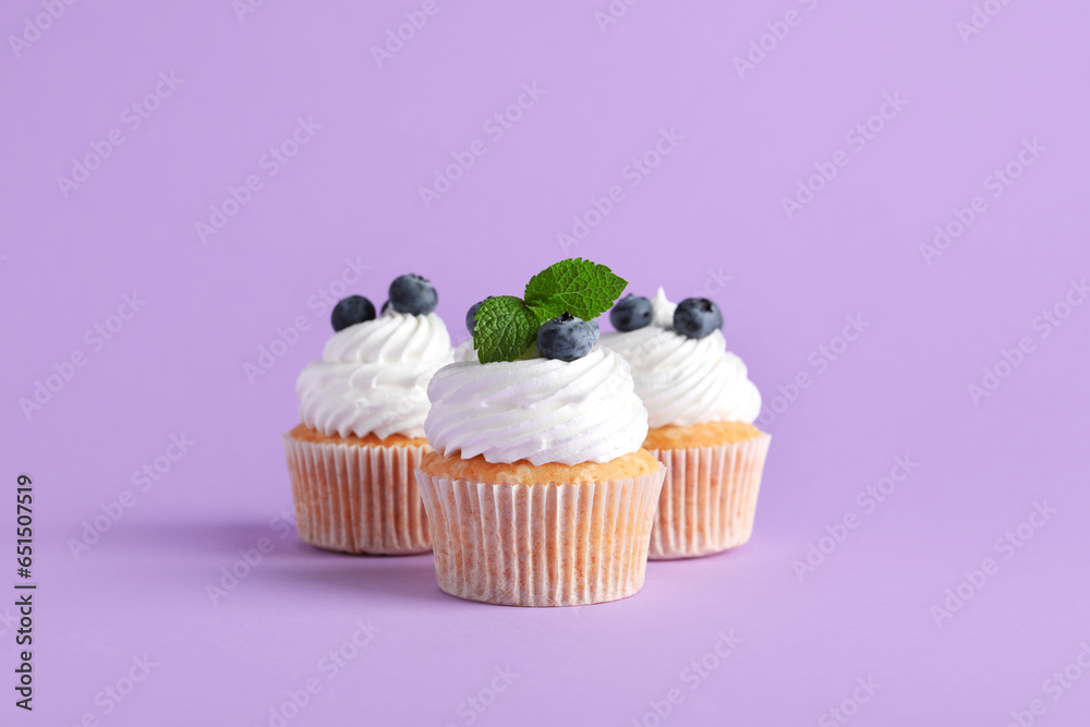 Tasty cupcakes with blueberries on lilac background