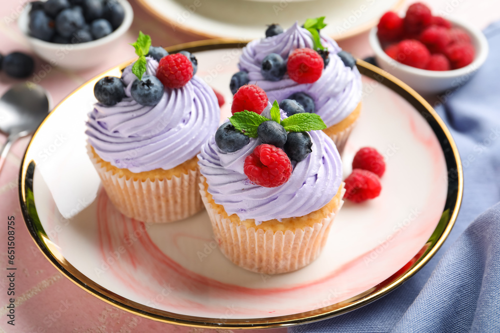 Plate of delicious cupcakes with blueberries, raspberries and mint on pink tile background