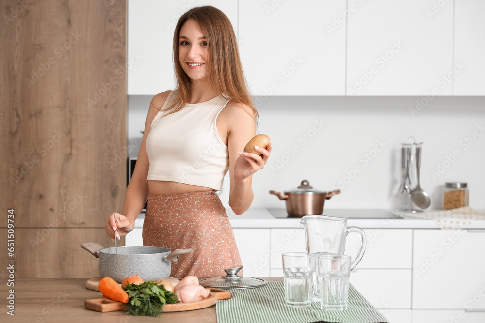 Young woman cooking chicken soup with vegetables in kitchen