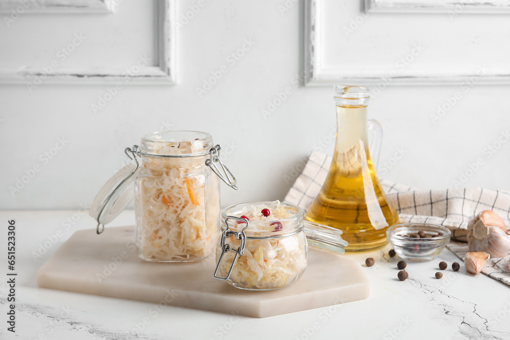 Board with jars of delicious sauerkraut and different spices on white background