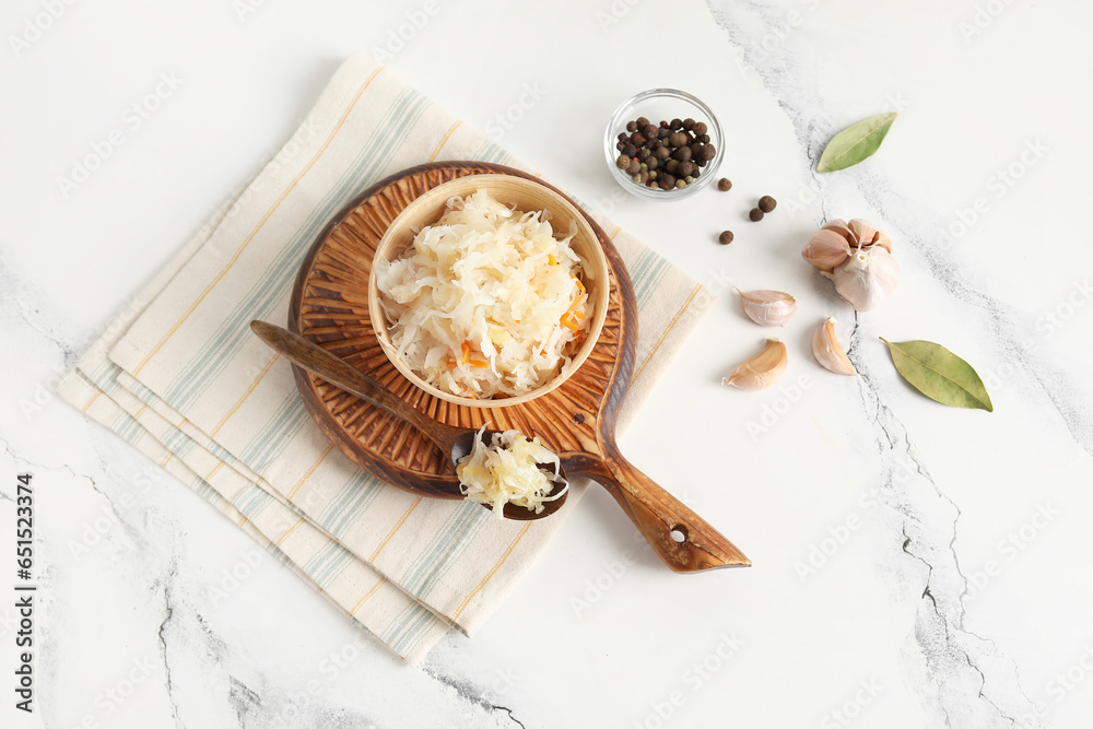 Bowl and spoon of delicious sauerkraut with different spices on white background