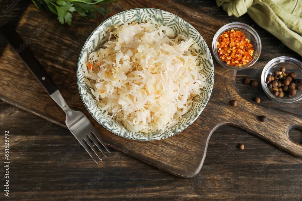 Bowl with delicious sauerkraut and different spices on wooden background