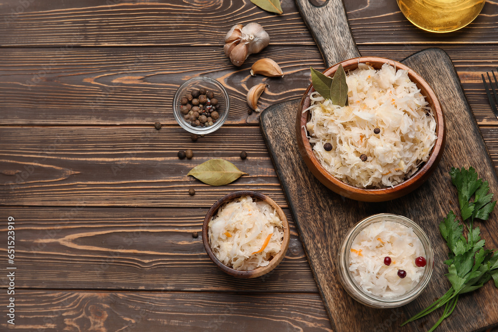 Bowls and jar of delicious sauerkraut with different spices on wooden background