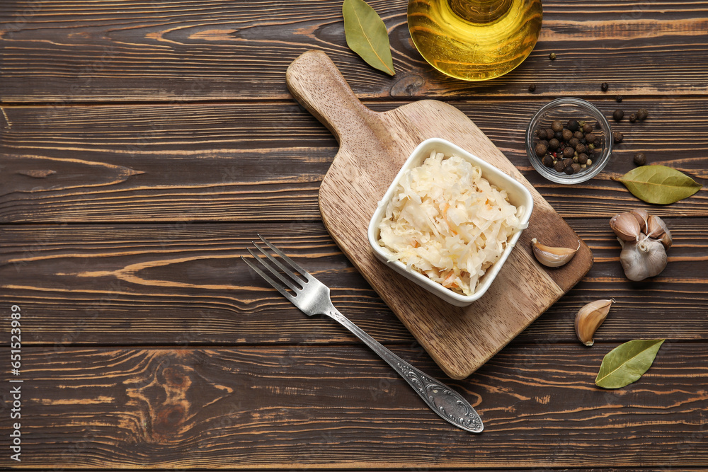 Board with bowl of delicious sauerkraut and different spices on wooden background