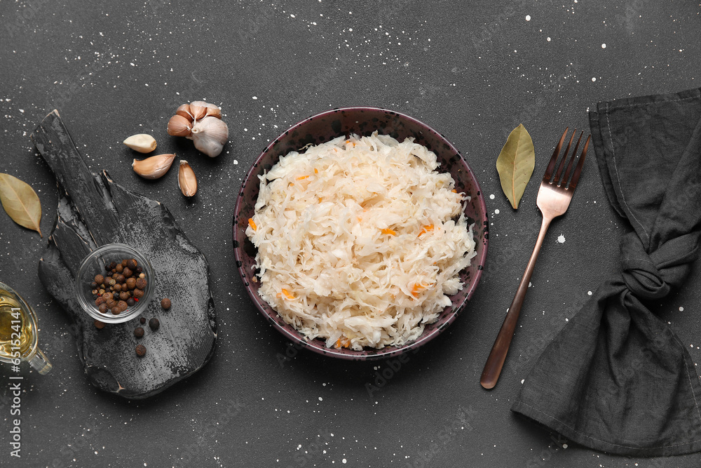 Bowl with delicious sauerkraut and different spices on black background