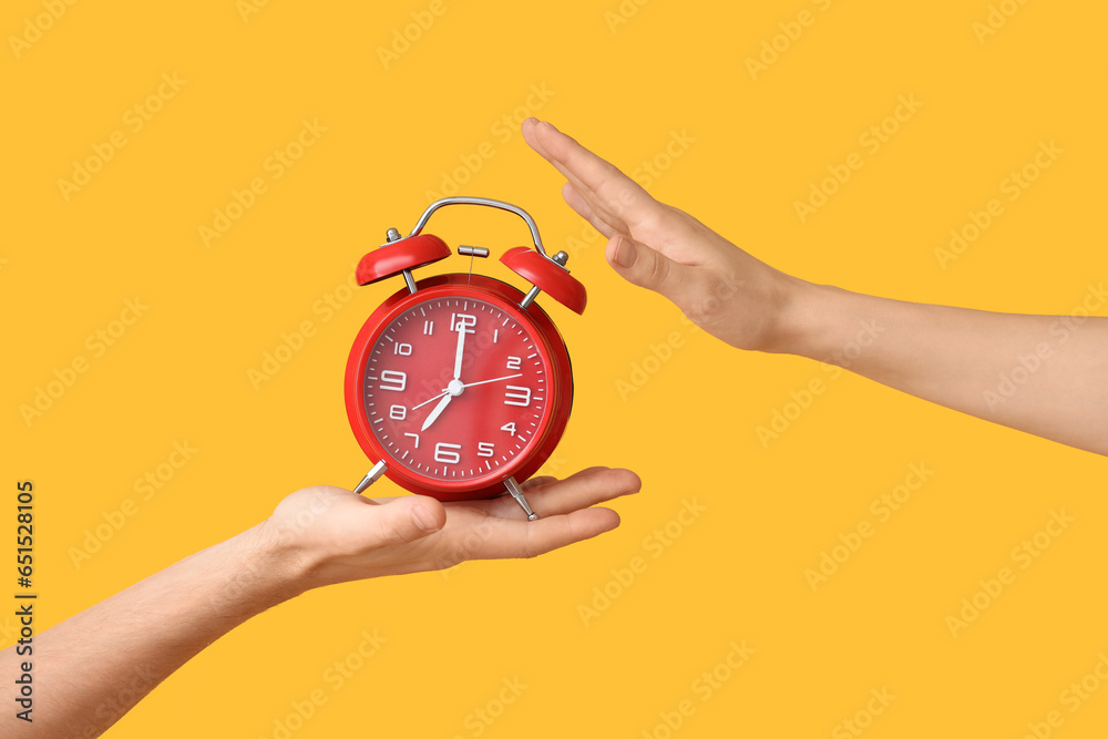 Hands holding alarm clock on yellow background