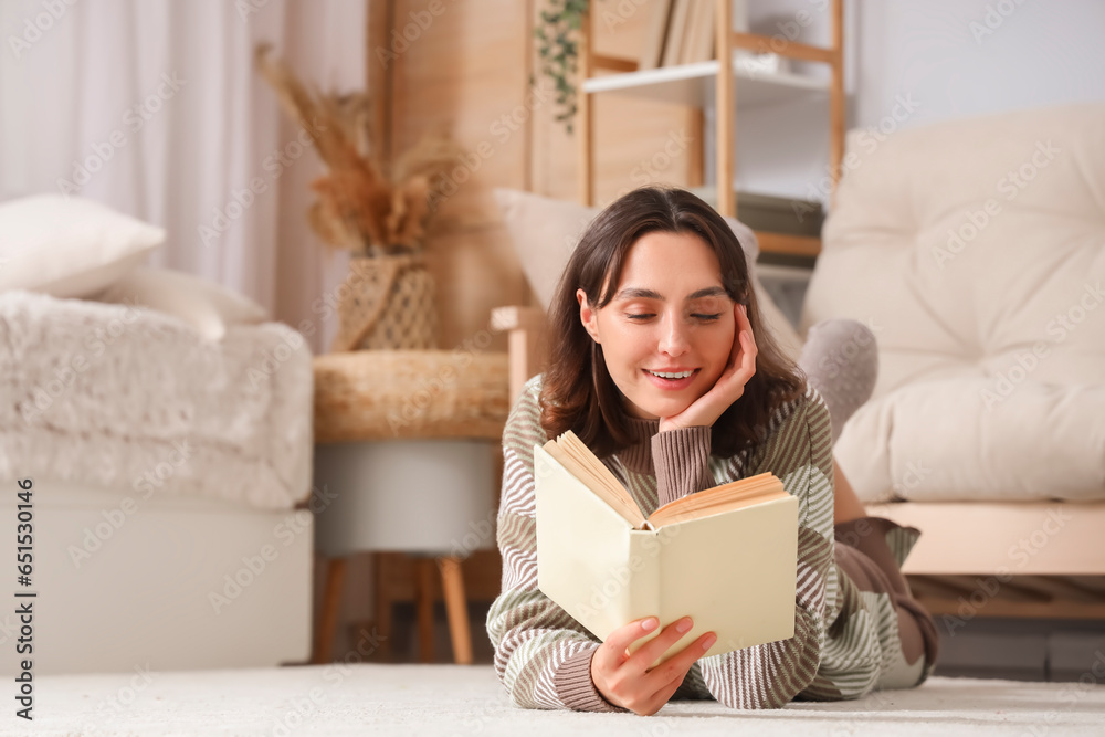 Young woman in warm sweater reading book at home