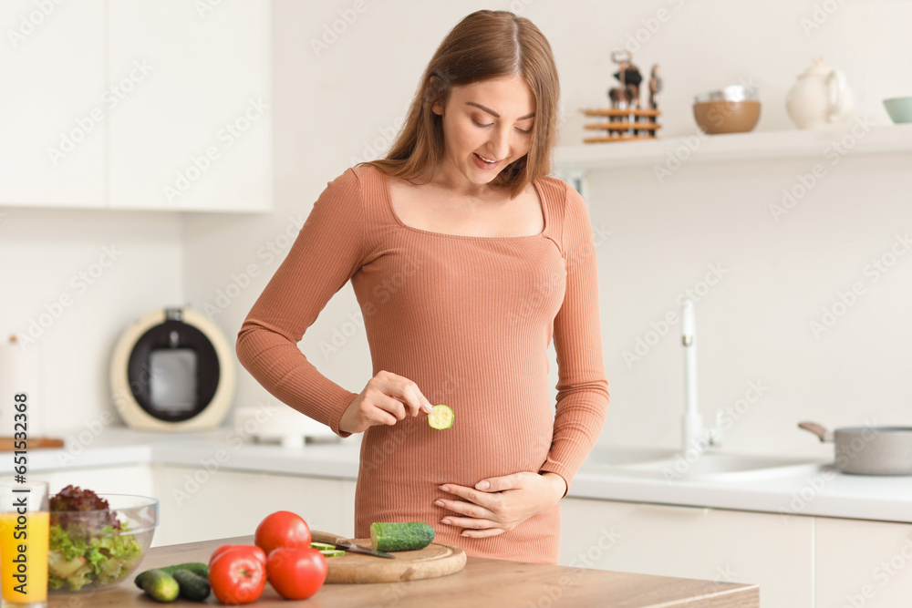 Young pregnant woman with cucumber slice in kitchen