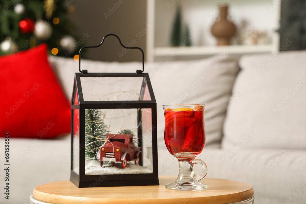 Glass of mulled wine with Christmas gift on table in living room, closeup