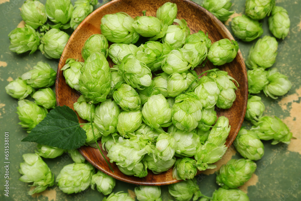 Wooden plate with fresh green hops and leaf on color background