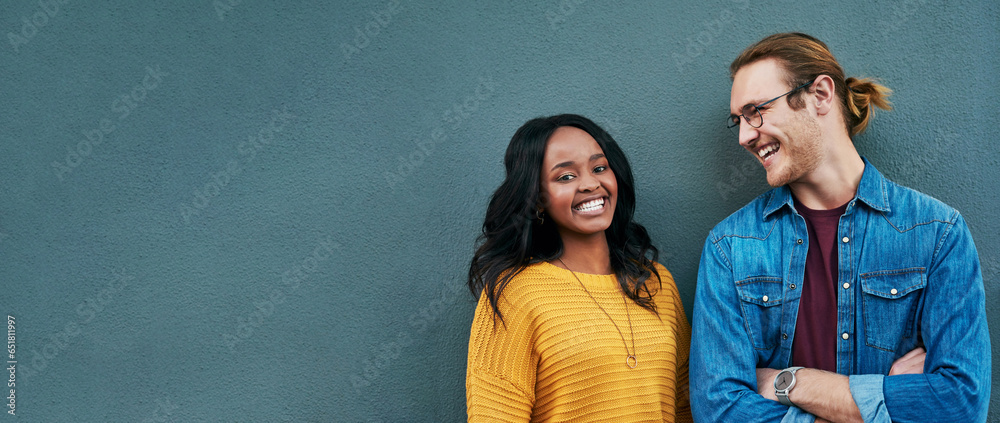 Happy, conversation and couple by wall with mockup space for advertising, promotion or marketing. Smile, talking and young interracial man and woman in discussion together by gray background mock up.