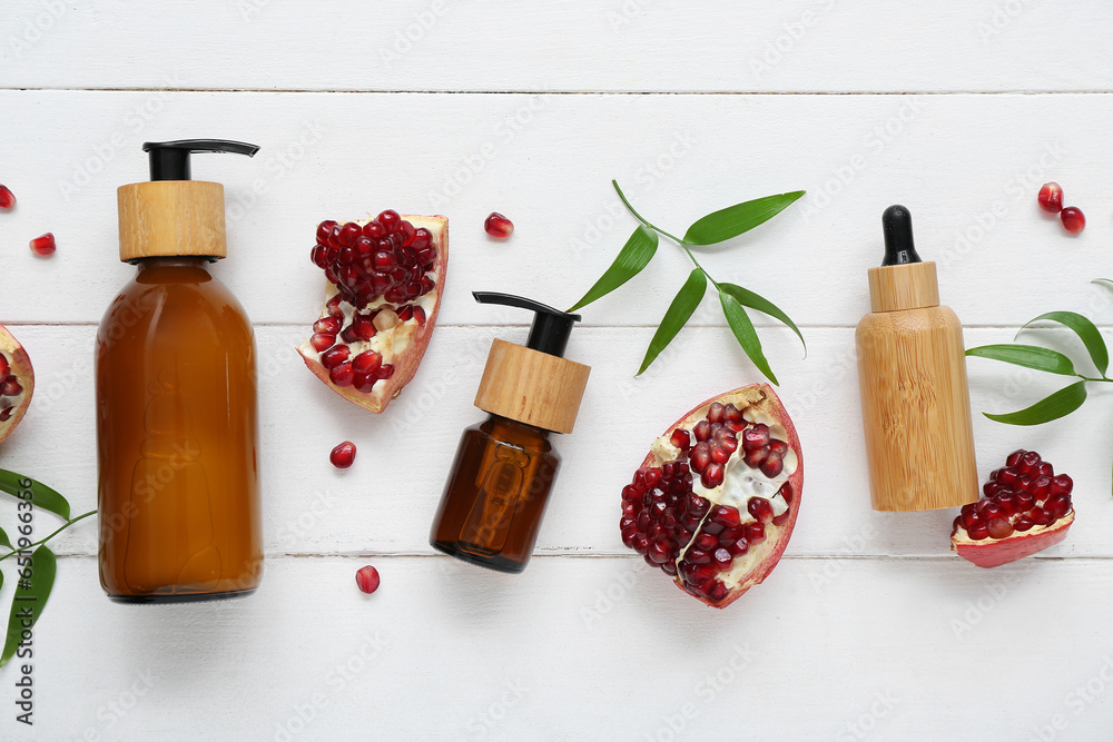 Composition with cosmetic products, pomegranate and plant leaves on light wooden background