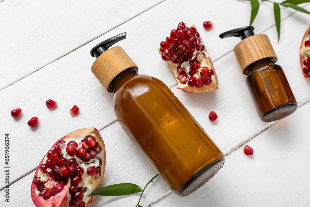 Bottles of cosmetic products and ripe pomegranate on light wooden background, closeup