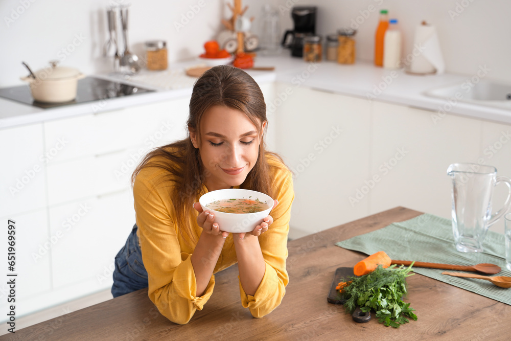 Young woman with bowl of chicken soup in kitchen