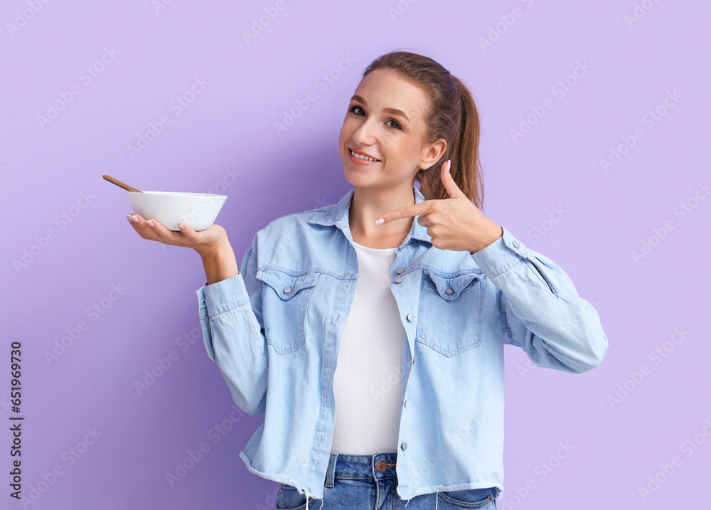 Young woman pointing at chicken soup on lilac background