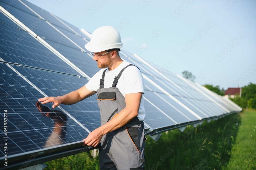 Male worker in uniform outdoors with solar batteries at sunny day.