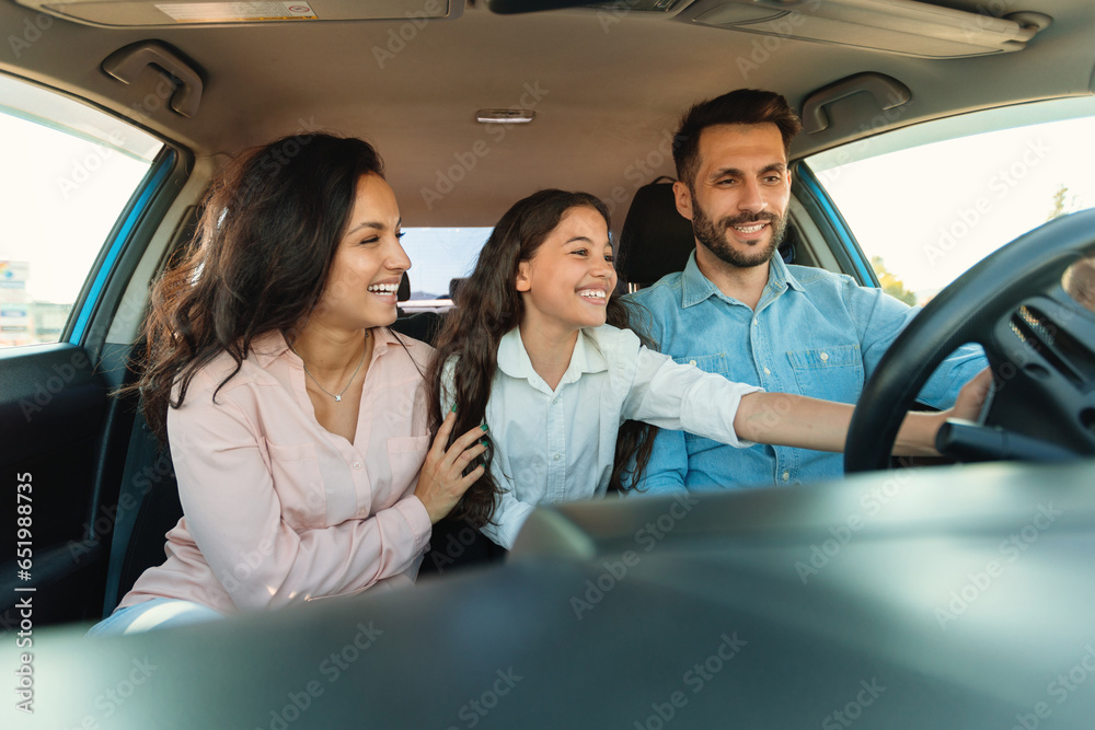 Happy parents and their child enjoying brand new car, girl touching wheel, sitting with mother and father inside auto