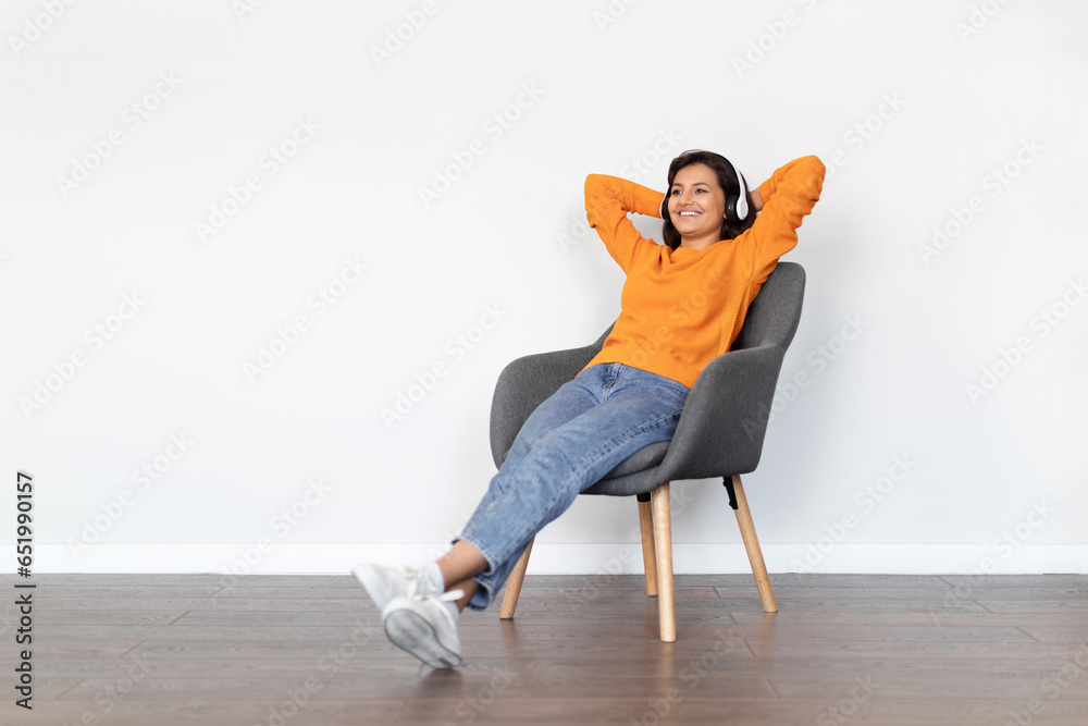 Relaxed young indian woman reclining on chair, listening to music