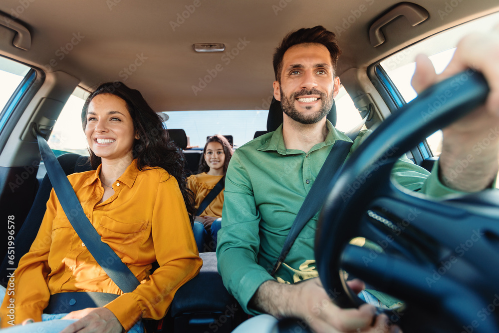 Young european parents and daughter riding new car and smiling, enjoying road trip together