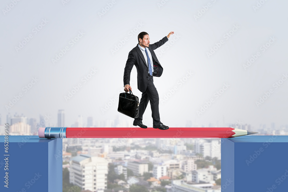 Attractive young european businessman crossing pencil bridge on sky background. Career problem and gap concept.