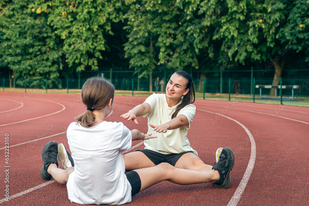 Caucasian woman and little girl are engaged in fitness at the stadium.