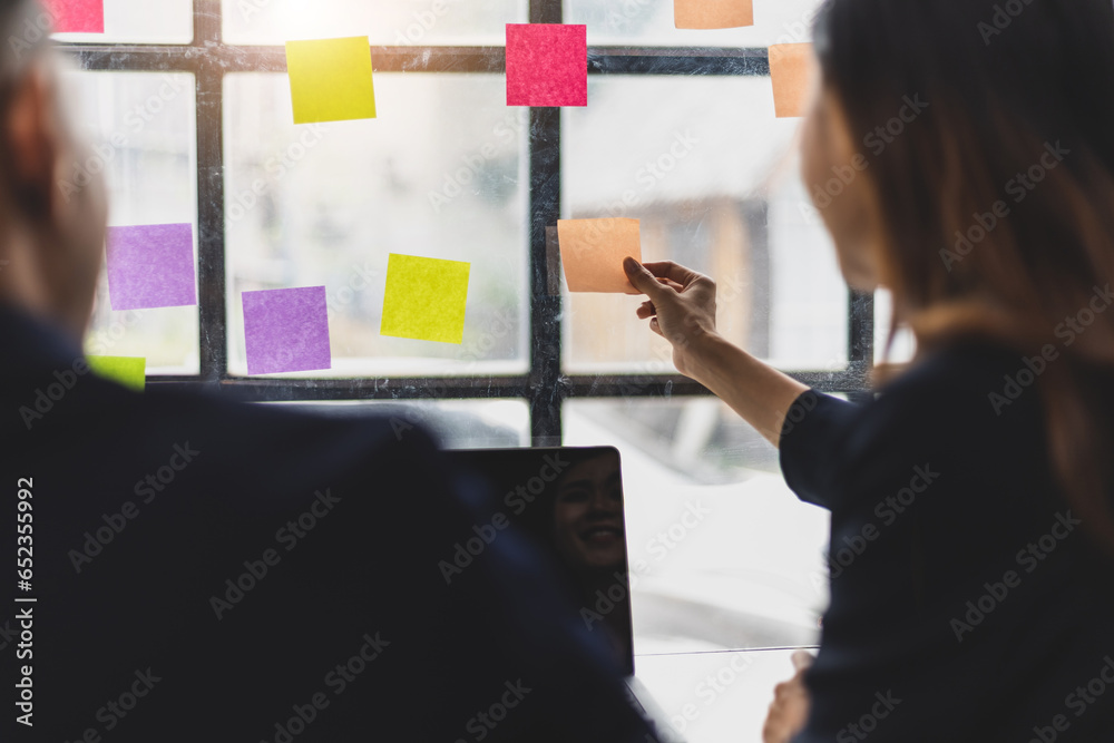 Businessmen and colleagues brainstorming scheduling business strategy, planning work in the office with paper stickers on the glass.