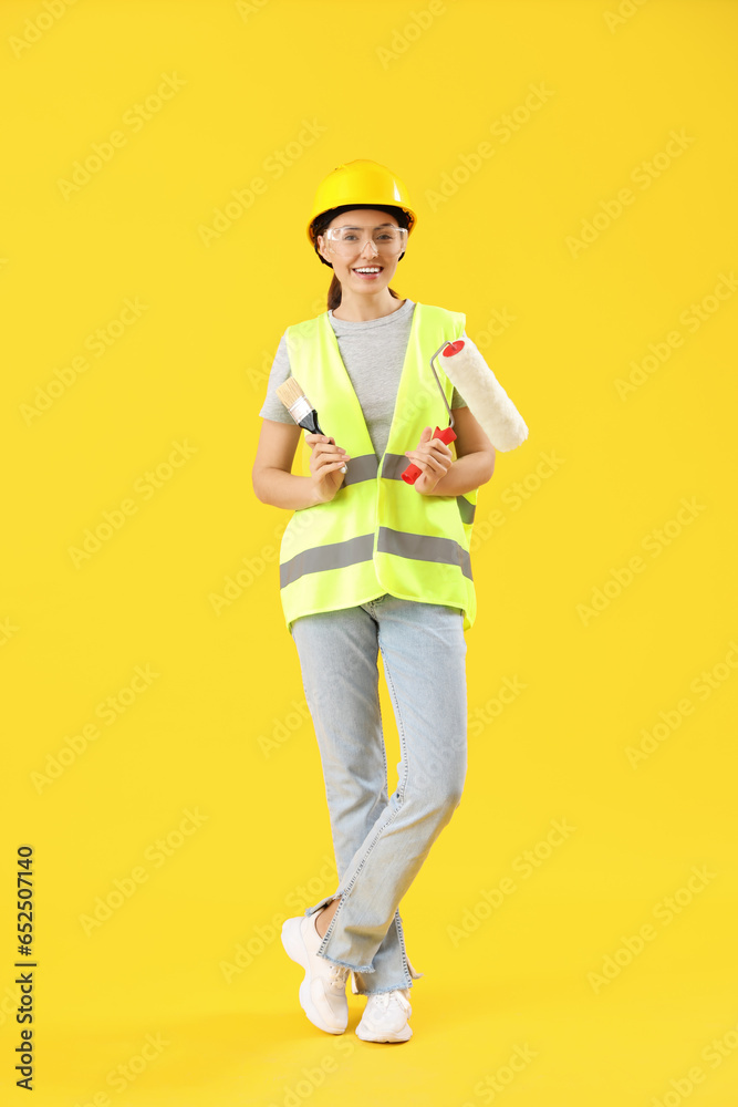 Female decorator with paint roller and brush on yellow background