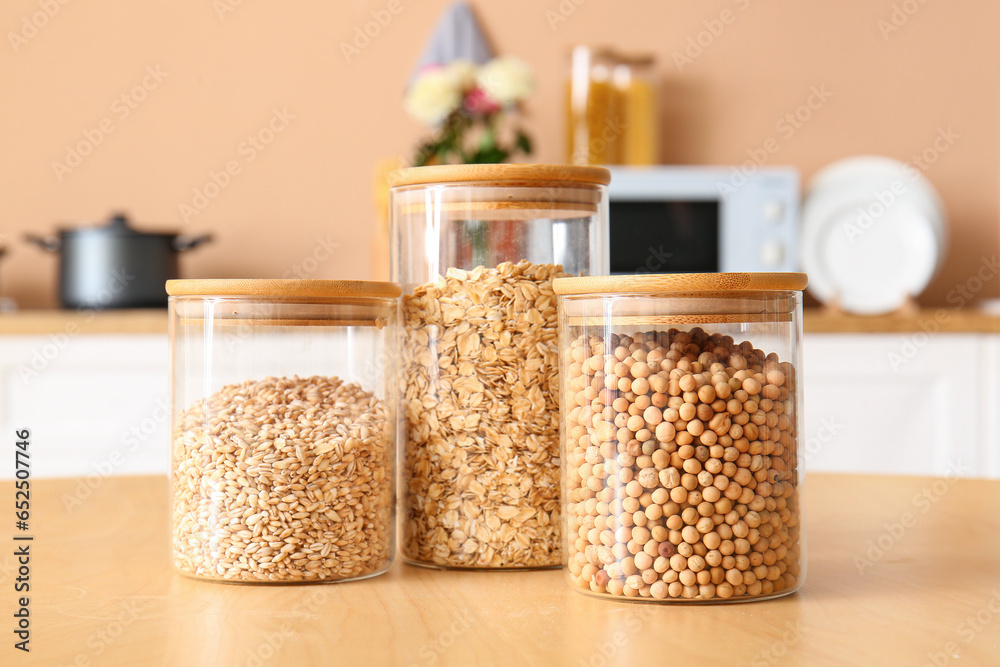 Glass jar with different cereals on wooden table in kitchen