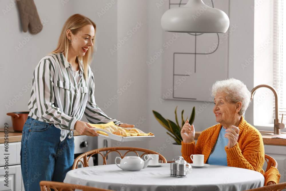 Young woman with baked croissants and her grandmother in kitchen