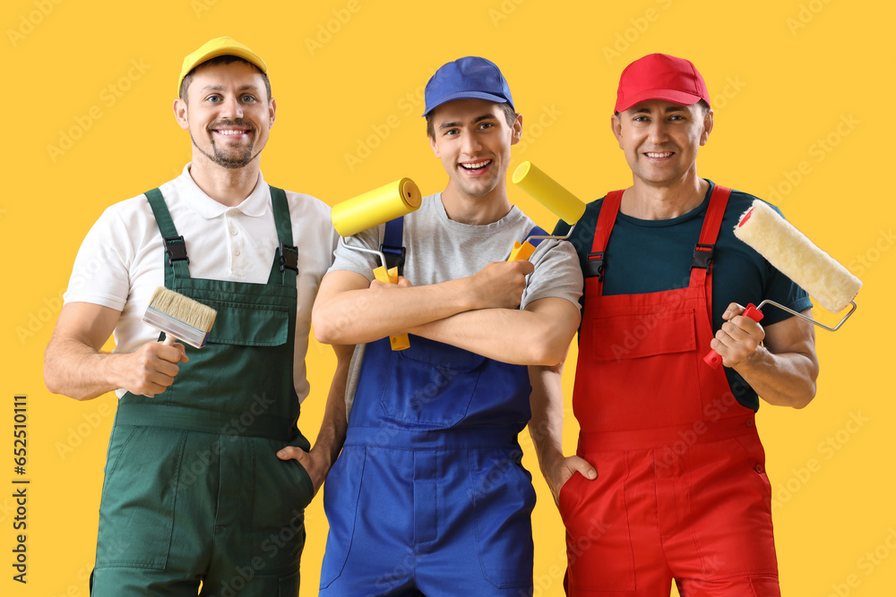 Team of male builders with paint rollers on yellow background