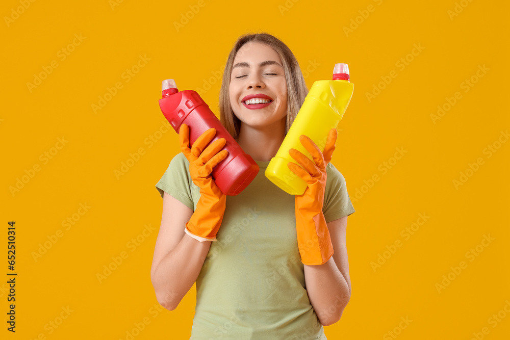 Young woman with bottles of detergent on orange background