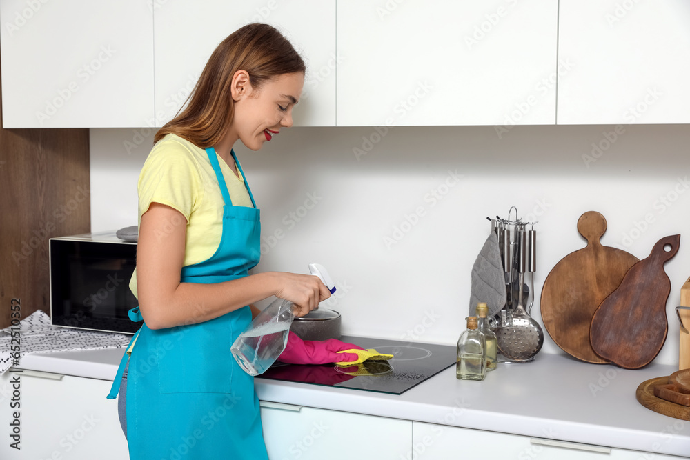 Young woman cleaning electric stove in kitchen