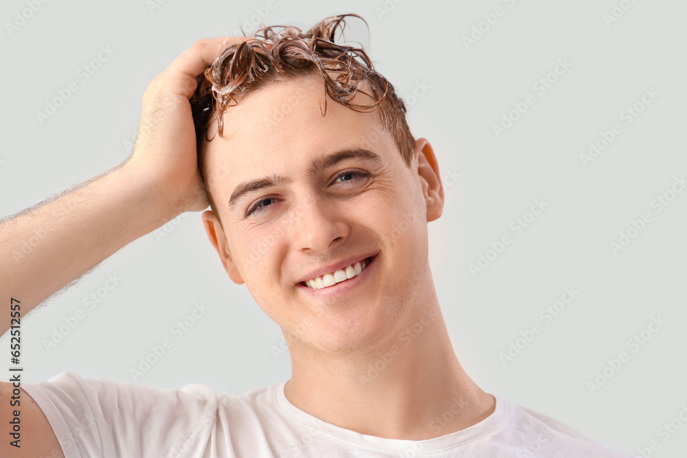 Young man washing hair against light background