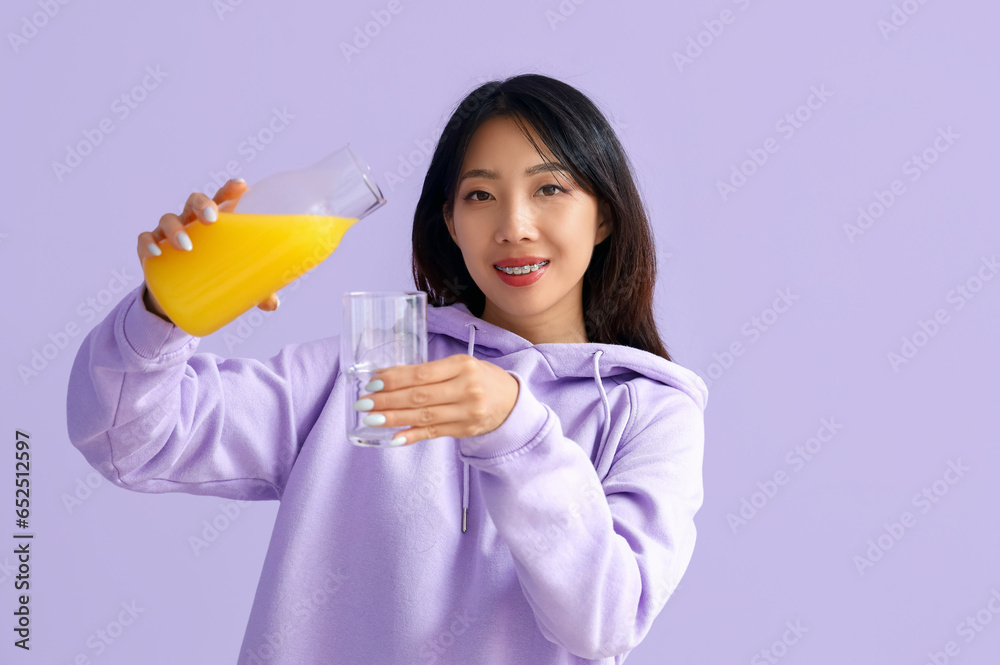 Beautiful Asian woman with glass and bottle of juice on lilac background