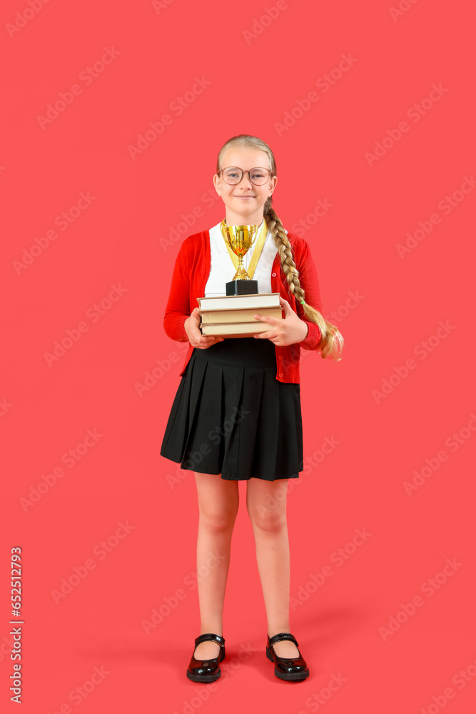 Cute little schoolgirl with gold cup and books on red background