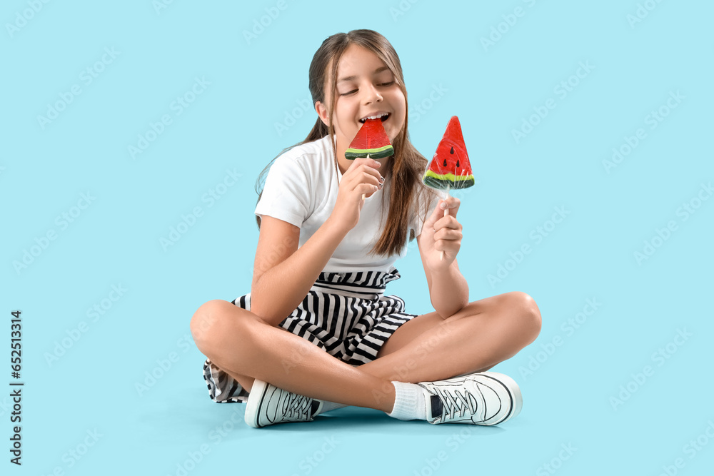 Happy little girl with lollipops in shape of watermelon slices sitting on blue background